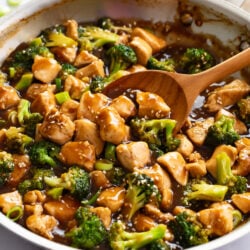 Chicken Teriyaki with broccoli in a skillet with a wooden spoon scooping it up.