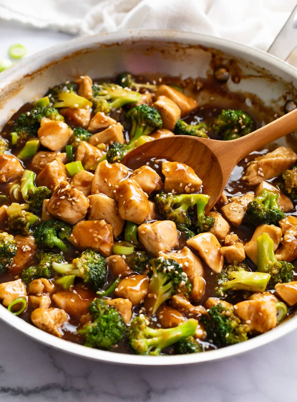 Chicken Teriyaki with broccoli in a skillet with a wooden spoon scooping it up.