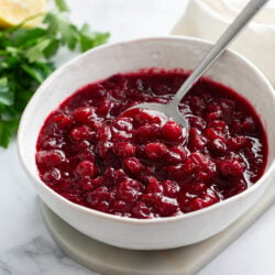 Homemade Cranberry Sauce in a white bowl with a spoon and parsley in the background.