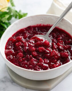 Homemade Cranberry Sauce in a white bowl with a spoon and parsley in the background.