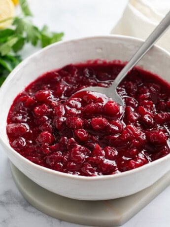 Homemade Cranberry Sauce in a white bowl with a spoon and parsley in the background.