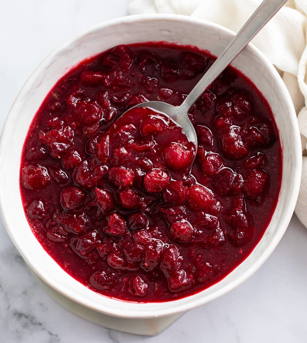 Cranberry Sauce in a white bowl with a spoon scooping it up.