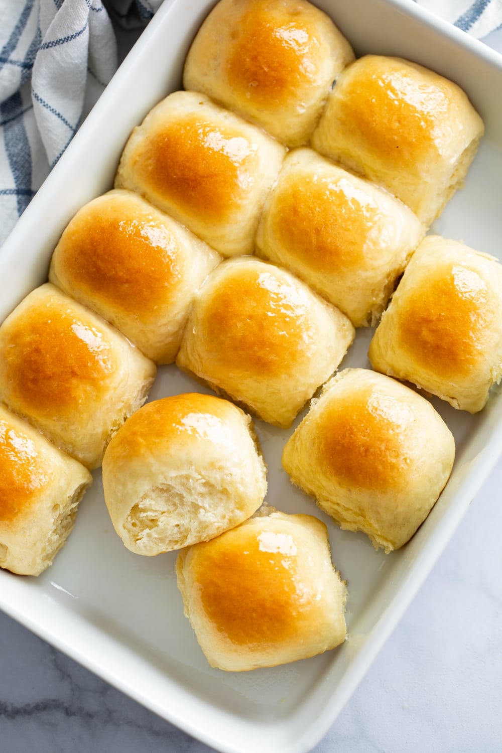 Fluffy Dinner Rolls in a white baking dish with honey butter on top.