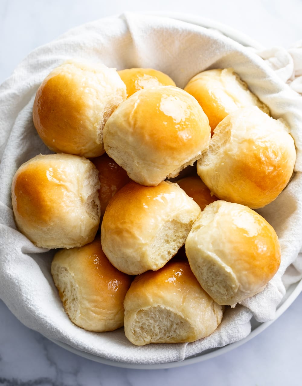 Dinner Rolls stacked up in a bowl with a white cloth.