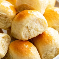 Light and fluffy dinner rolls stacked on a white plate.