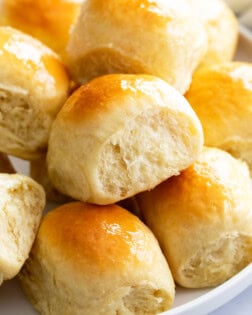 Light and fluffy dinner rolls stacked on a white plate.