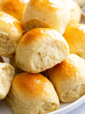 Light and fluffy dinner rolls stacked on a white plate.