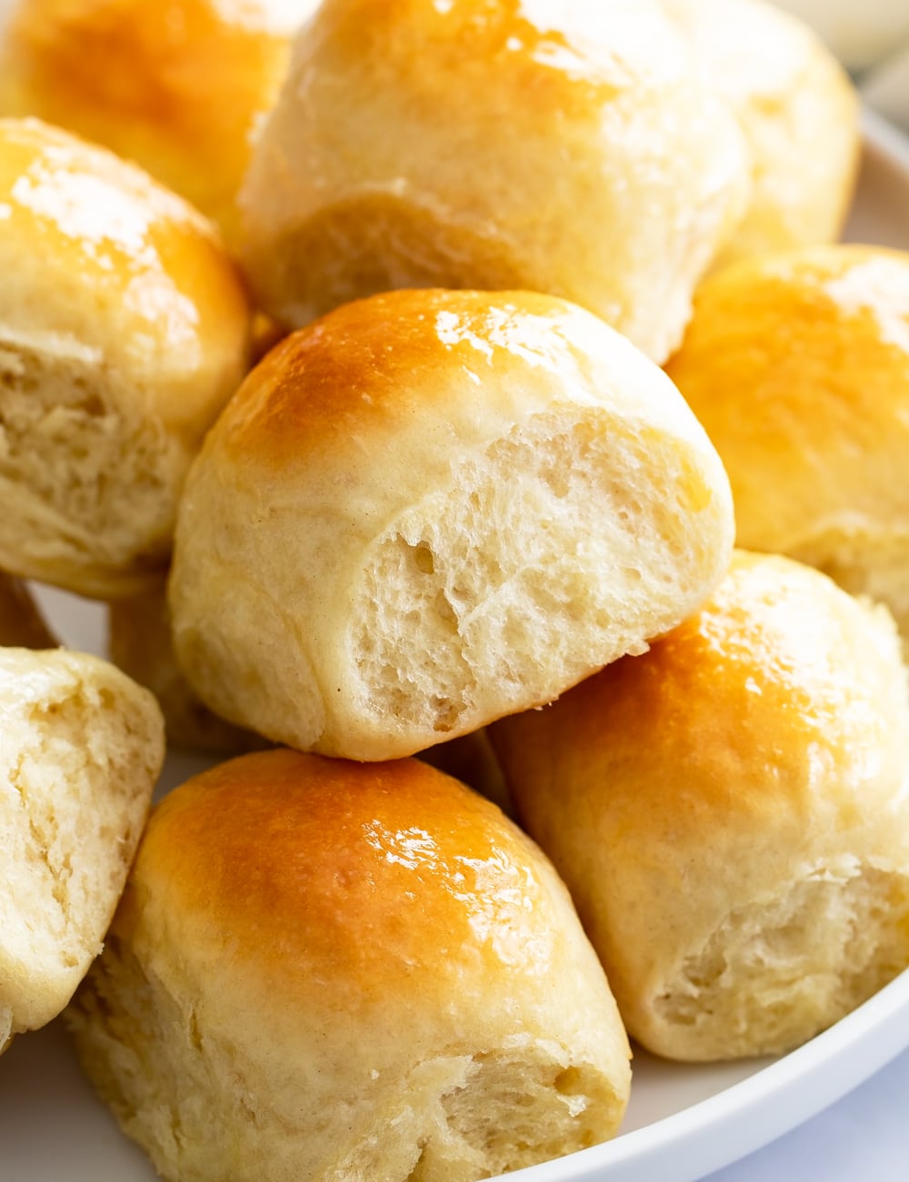 Light and fluffy dinner rolls stacked on a white plate.