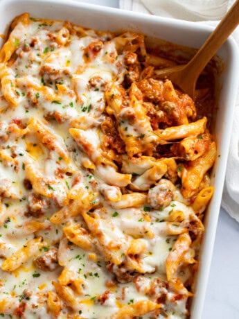 Ground Beef Casserole in a white baking dish with a wooden spoon scooping it out.