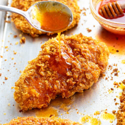 A spoon drizzling honey on top of crispy chicken.