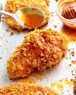 A spoon drizzling honey on top of crispy chicken.