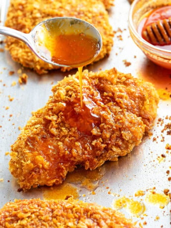 A spoon drizzling honey on top of crispy chicken.