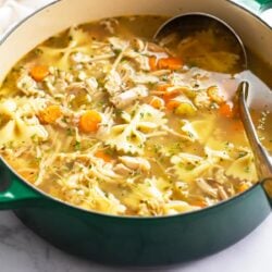 Turkey Soup in a green soup pot with vegetables, turkey, and pasta.