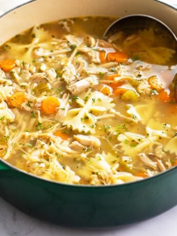 Turkey Soup in a green soup pot with vegetables, turkey, and pasta.