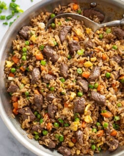 Beef Fried Rice in a skillet with peas and carrots and a spoon.