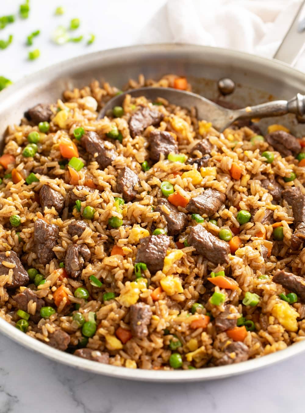 A skillet with Beef Fried Rice with vegetables and green onions.