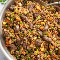 Beef Fried Rice in a skillet with vegetables, beef, green onions, and a spoon on the side.