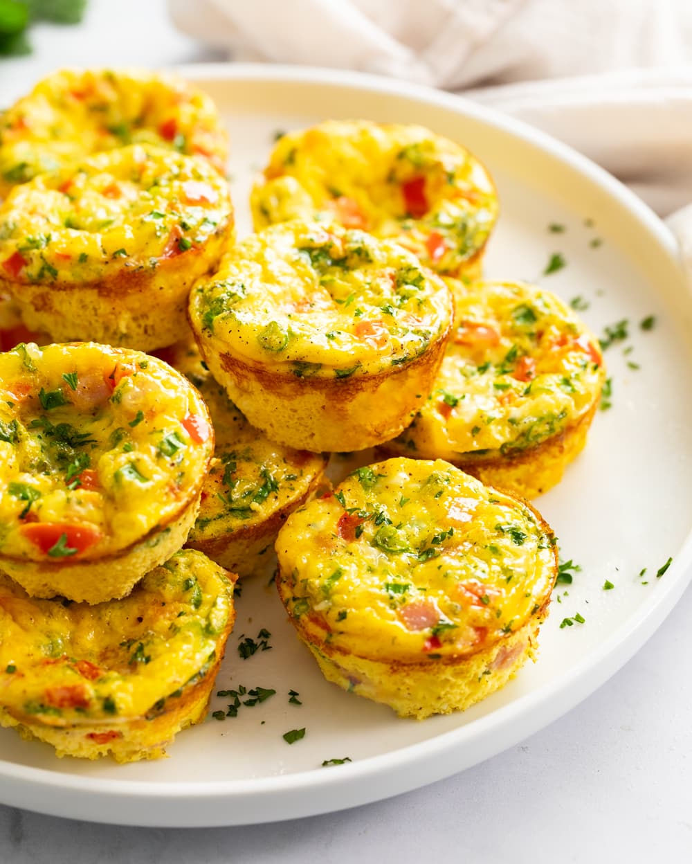 Egg muffins stacked on top of each other on a white plate with chopped parsley.