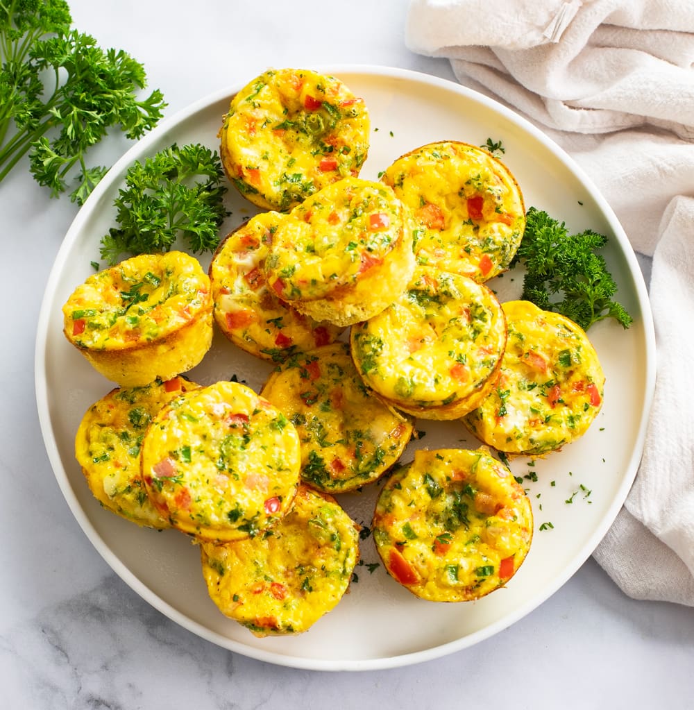 Egg Muffins on a white plate with parsley and colorful fillings.