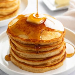 A stack of Homemade Pancakes on a white plate with syrup being poured on top.