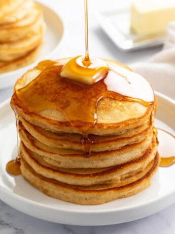 A stack of Homemade Pancakes on a white plate with syrup being poured on top.