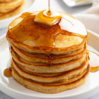 A stack of Homemade Pancakes on a white plate with butter and syrup.