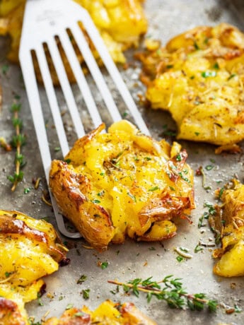 A spatula scooping up a smashed potato from a baking sheet.