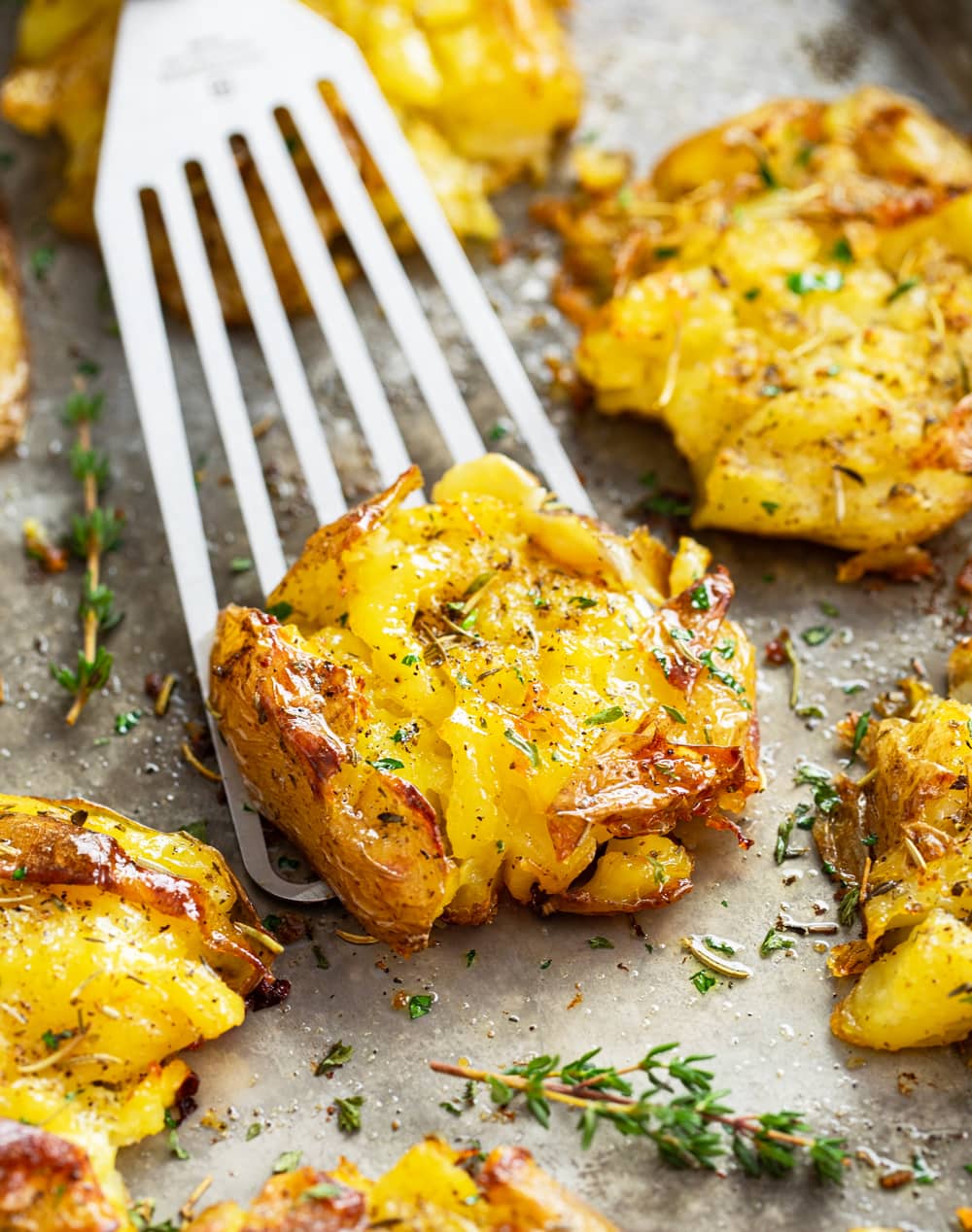 A spatula scooping up a smashed potato from a baking sheet.