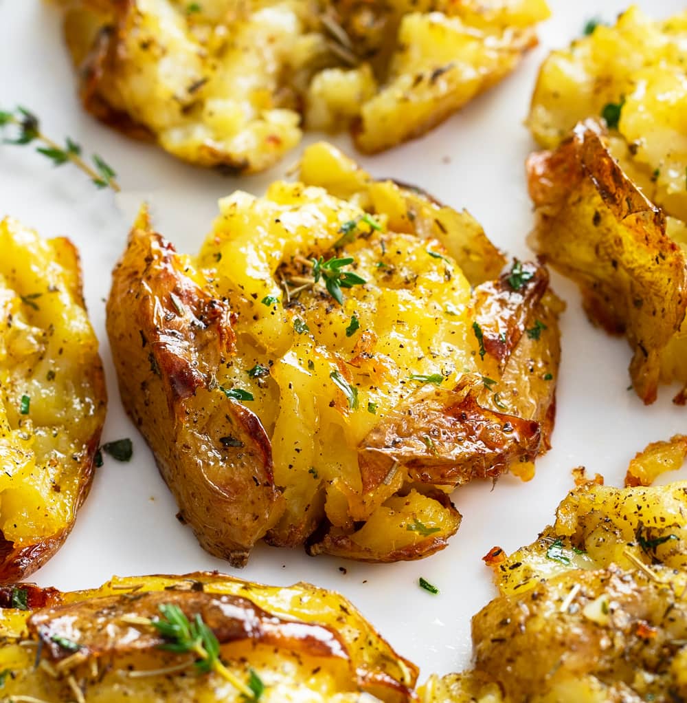 A Smashed Potato on a white plate with fresh thyme and seasonings.