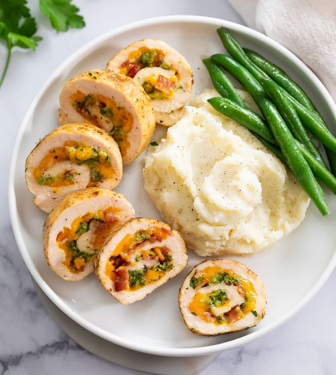 Slices of Chicken Roulade on a white plate with mashed potatoes and green beans.