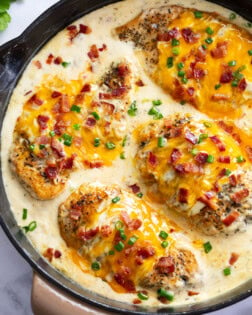 A skillet of Bacon Ranch Chicken with cheese, bacon and green onions on top.