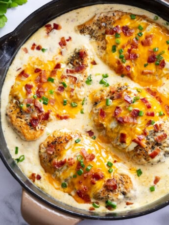 A skillet of Bacon Ranch Chicken with cheese, bacon and green onions on top.