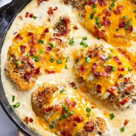 A skillet of Bacon Ranch Chicken with cheese, bacon and green onions on top.