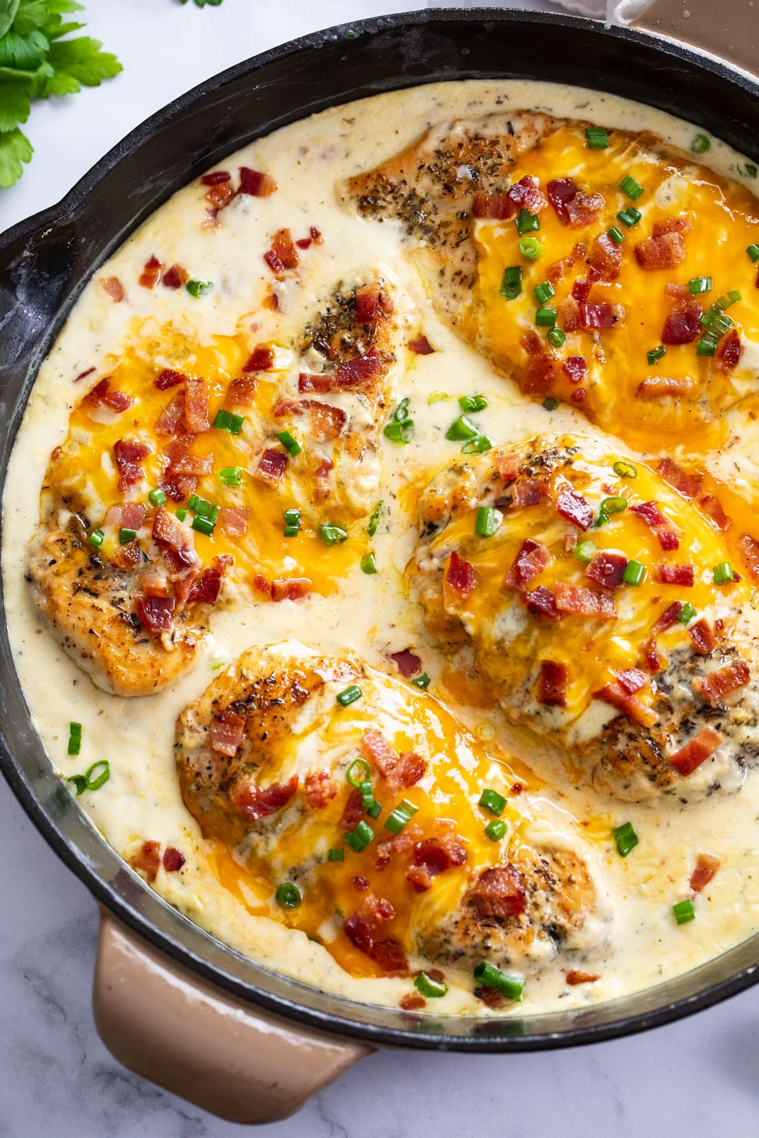A skillet of Bacon Ranch Chicken with cheese, bacon and green onions on top.
