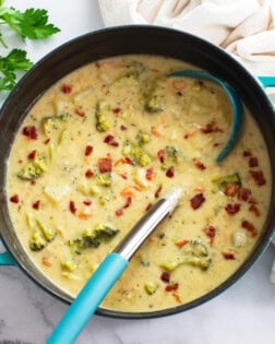 A soup pot of Broccoli Potato Soup with bacon on top and a ladle on the side.