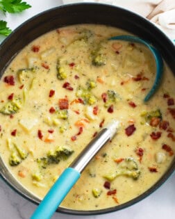 A pot of Broccoli Potato Soup with a soup ladle and bacon on top.