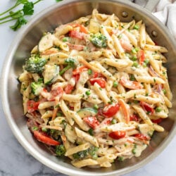 Pasta primavera in a skillet with a cream sauce and vegetables.