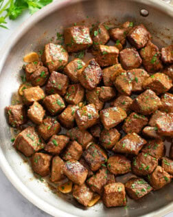 Steak Bites in a skillet in a Garlic Butter Sauce with parley on top.