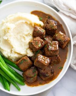 Steak Bites in a garlic butter sauce on a plate with mashed potatoes and green beans.