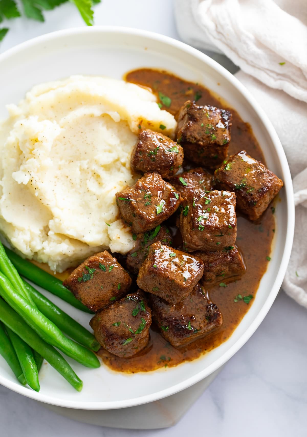Steak Bites in a garlic butter sauce on a plate with mashed potatoes and green beans.