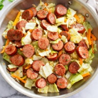 A skillet of Cabbage and Sausage with sliced carrots.