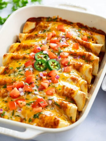 Chicken Enchiladas in a casserole dish with cheese and toppings on top.