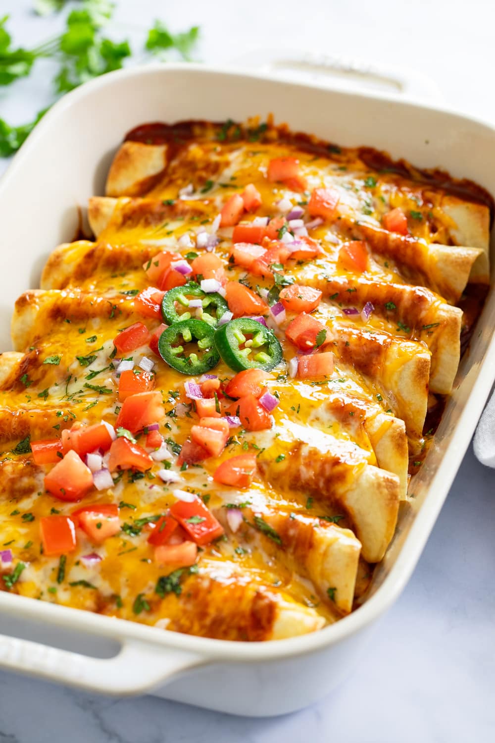 Chicken Enchiladas in a casserole dish with cheese and toppings on top.