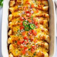 Chicken Enchiladas in a casserole dish with toppings and cheese on top.