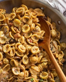 A wooden spoon scooping up French Onion Pasta from a skillet.