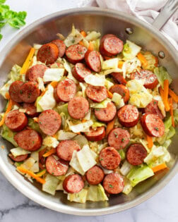 Cabbage and Sausage in a skillet with slices of carrots and parsley.