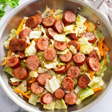 Cabbage and Sausage in a skillet with slices of carrots and parsley.