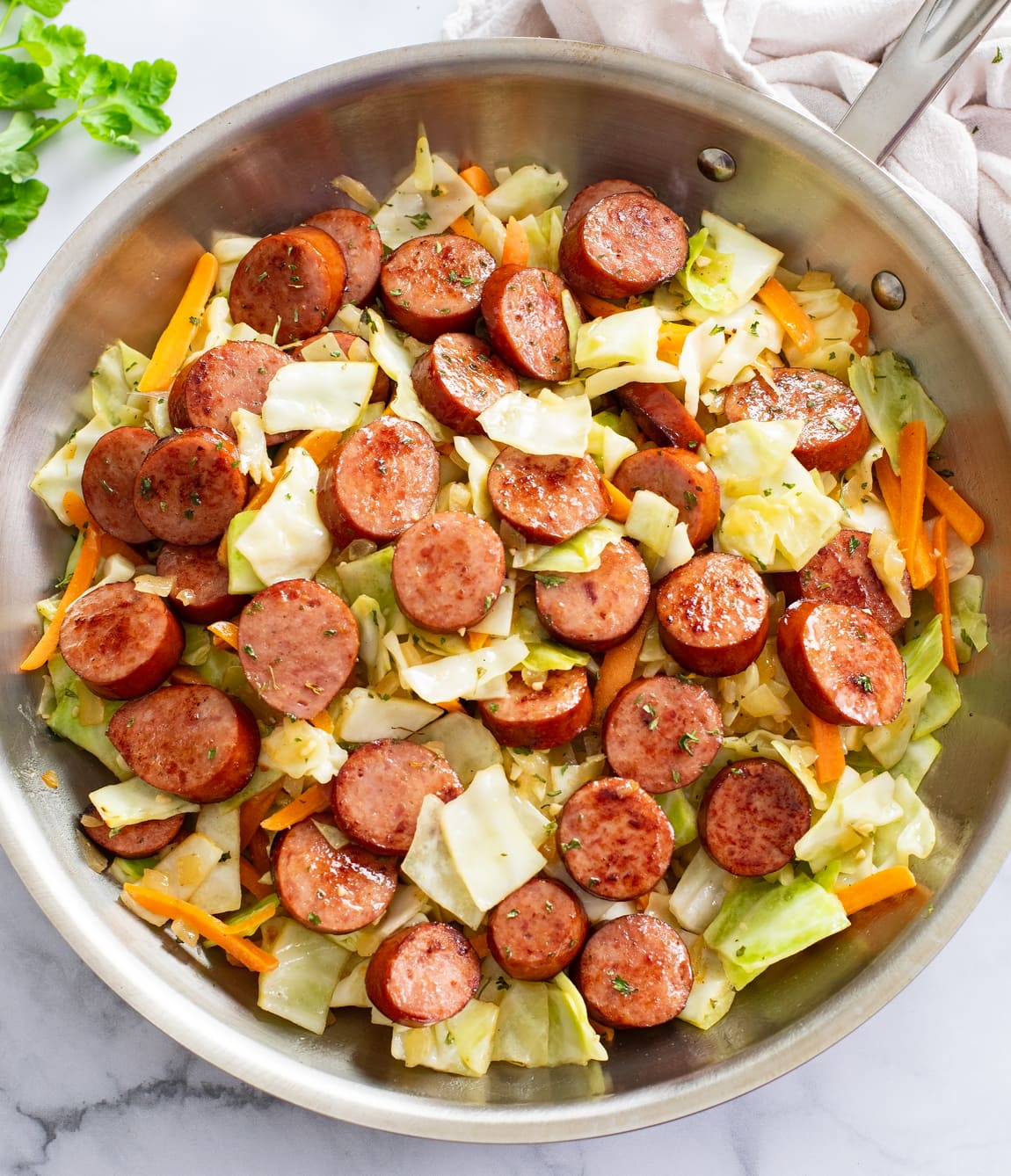 Cabbage and Sausage in a skillet with slices of carrots and parsley.