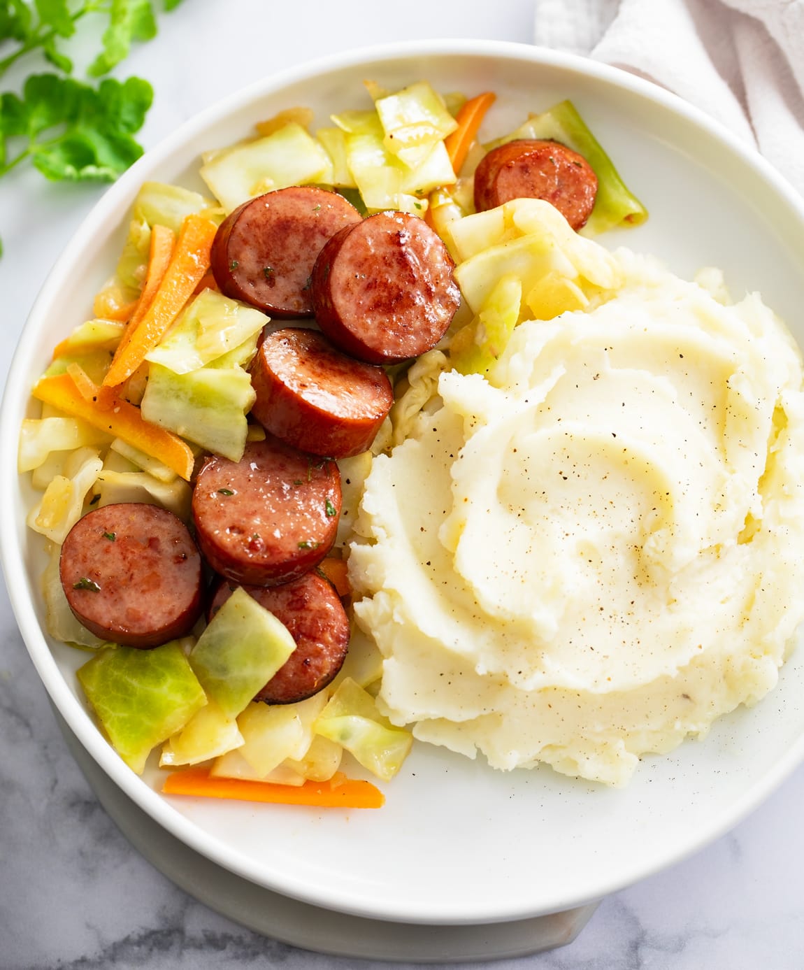 Cabbage and Sausage on a white plate with mashed potatoes on the side.