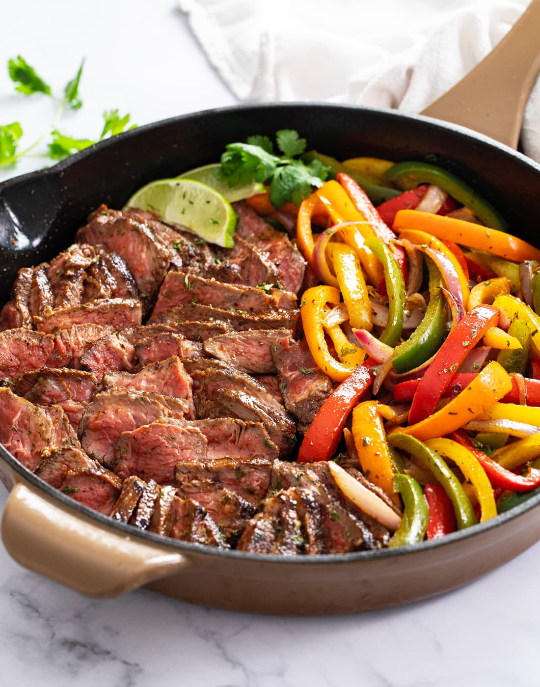 A skillet filled with Steak Fajitas with onions, peppers, and steak.